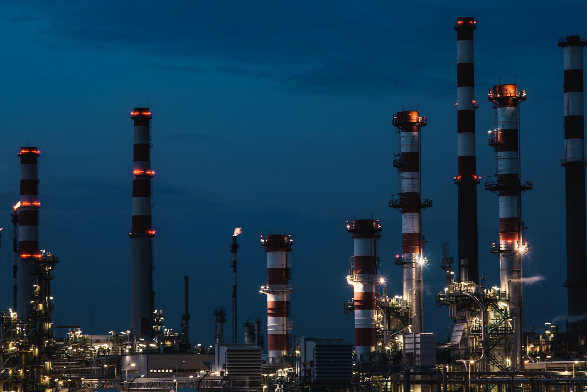 An industrial refinery with lit stacks at dusk